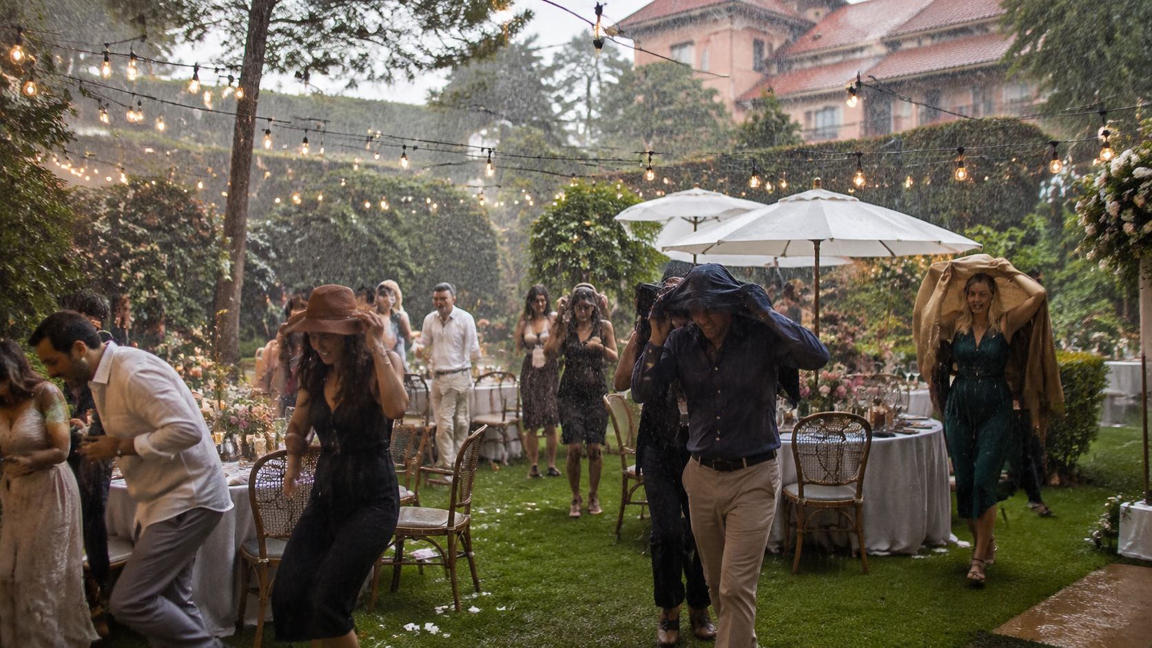 Invitados a una boda corriendo bajo la lluvia intensa mientras celebran un evento al aire libre.