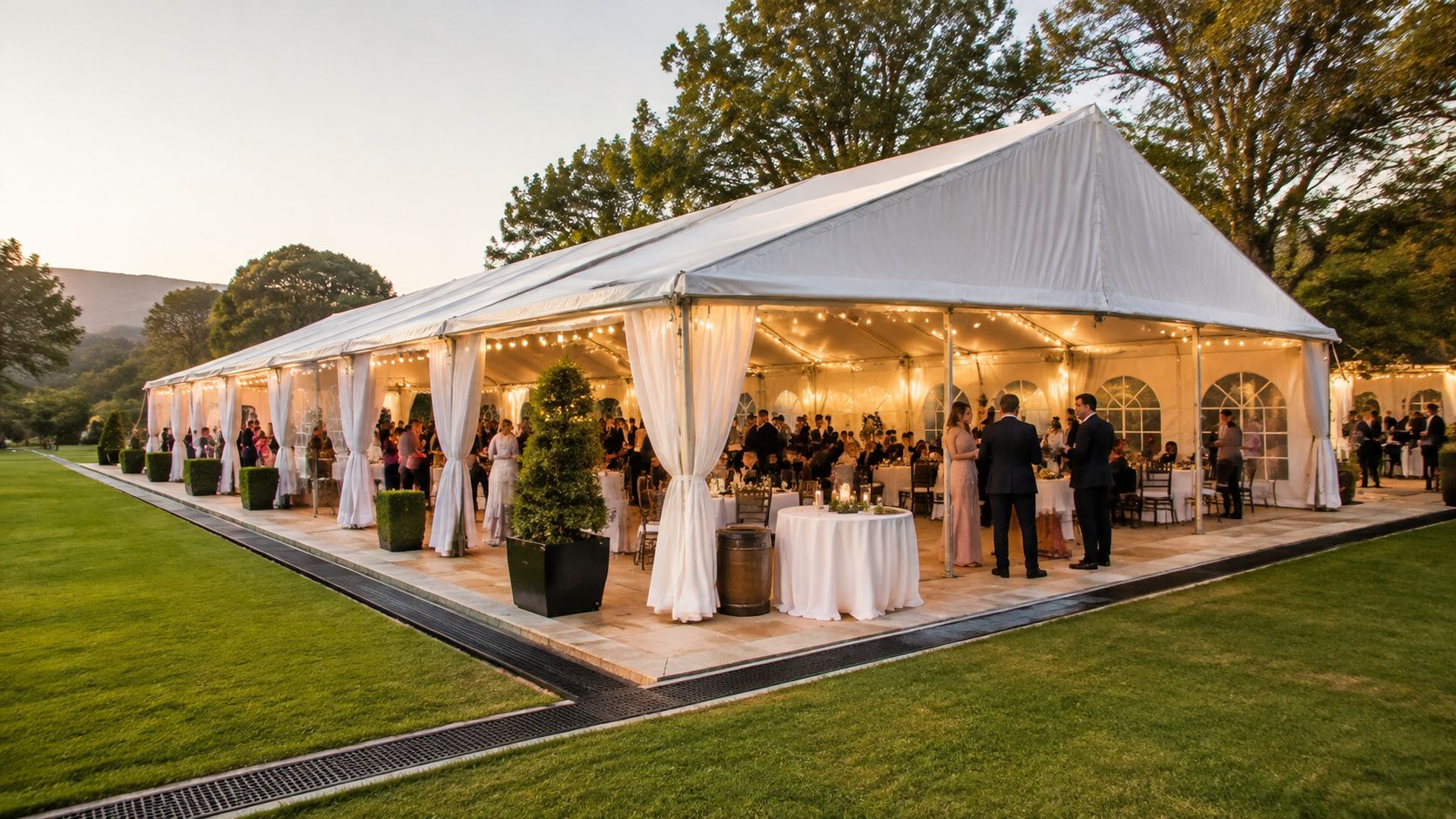 Elegante carpa blanca para eventos en un jardín al atardecer con invitados y decoración sofisticada.